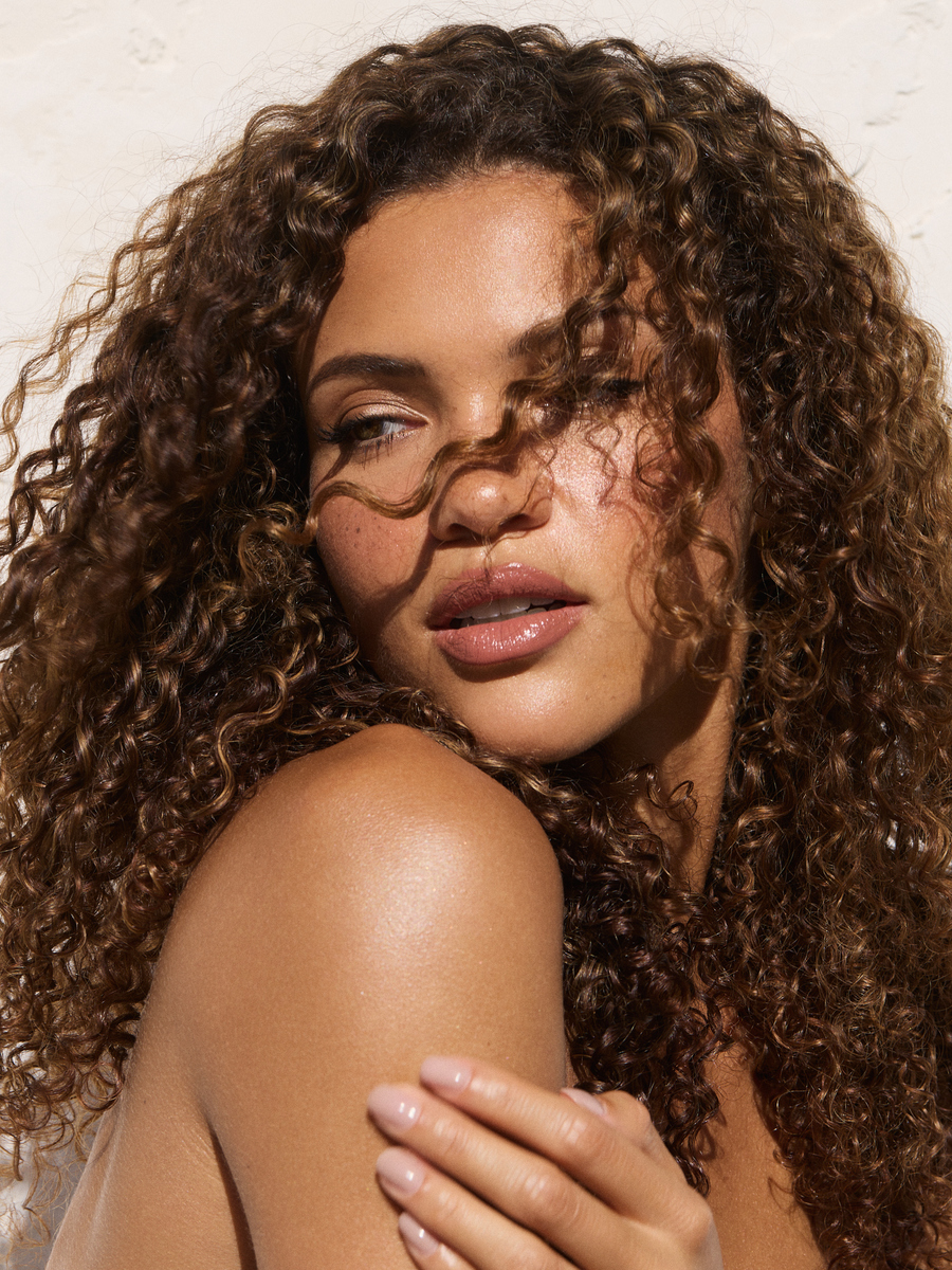 Close-up natural beauty portrait of a model with curly hair, freckles, luminous skin, and soft neutral makeup, photographed in Miami by Josh Eskridge.