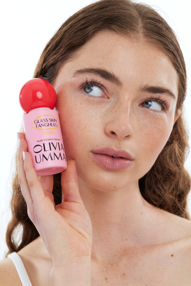 Model holding Olivia Umma Glass Skin Tanghulu multivitamin serum beside her face in a bright skincare beauty portrait.