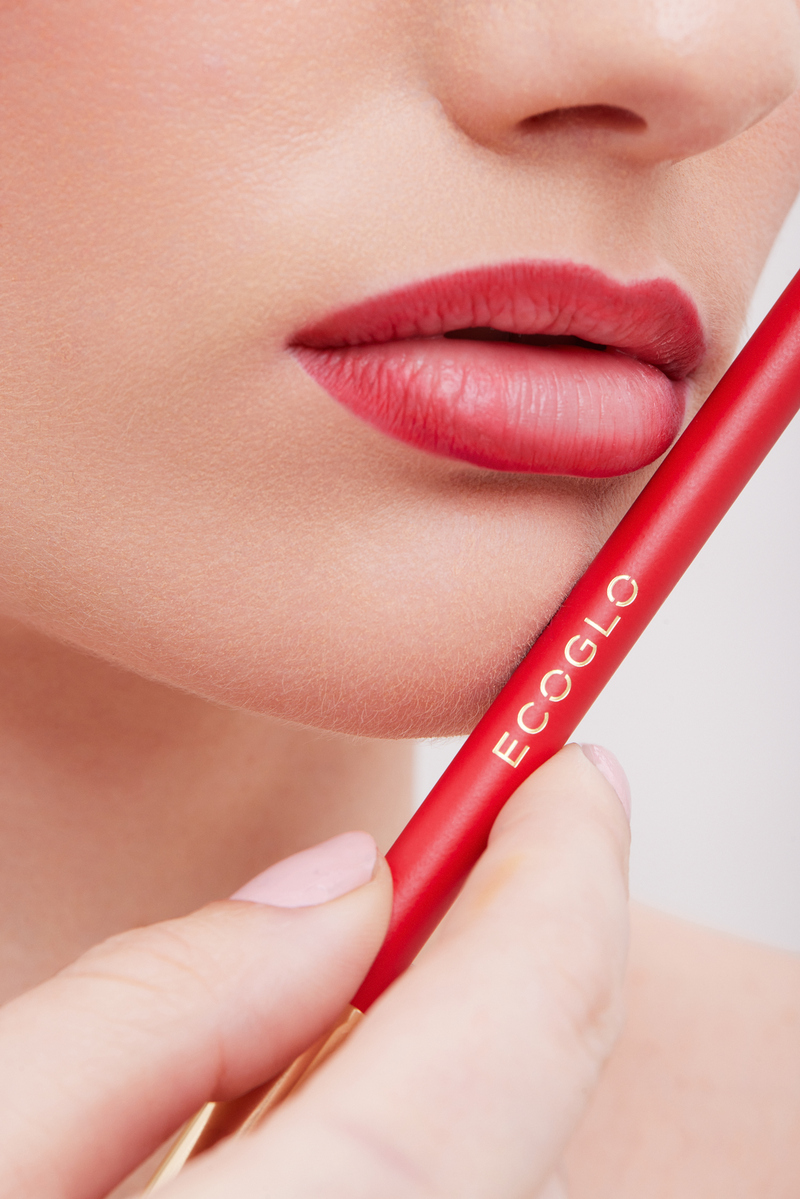 Macro beauty photograph of a model wearing red ombré lip color beside an Ecoglo lip liner pencil, photographed at Know Good Studio in Miami.