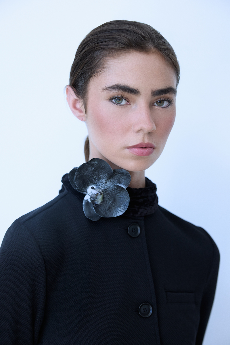 Editorial fashion portrait of a brunette model wearing a structured black jacket with a black floral accent, photographed at Know Good Studio in Miami by Josh Eskridge.