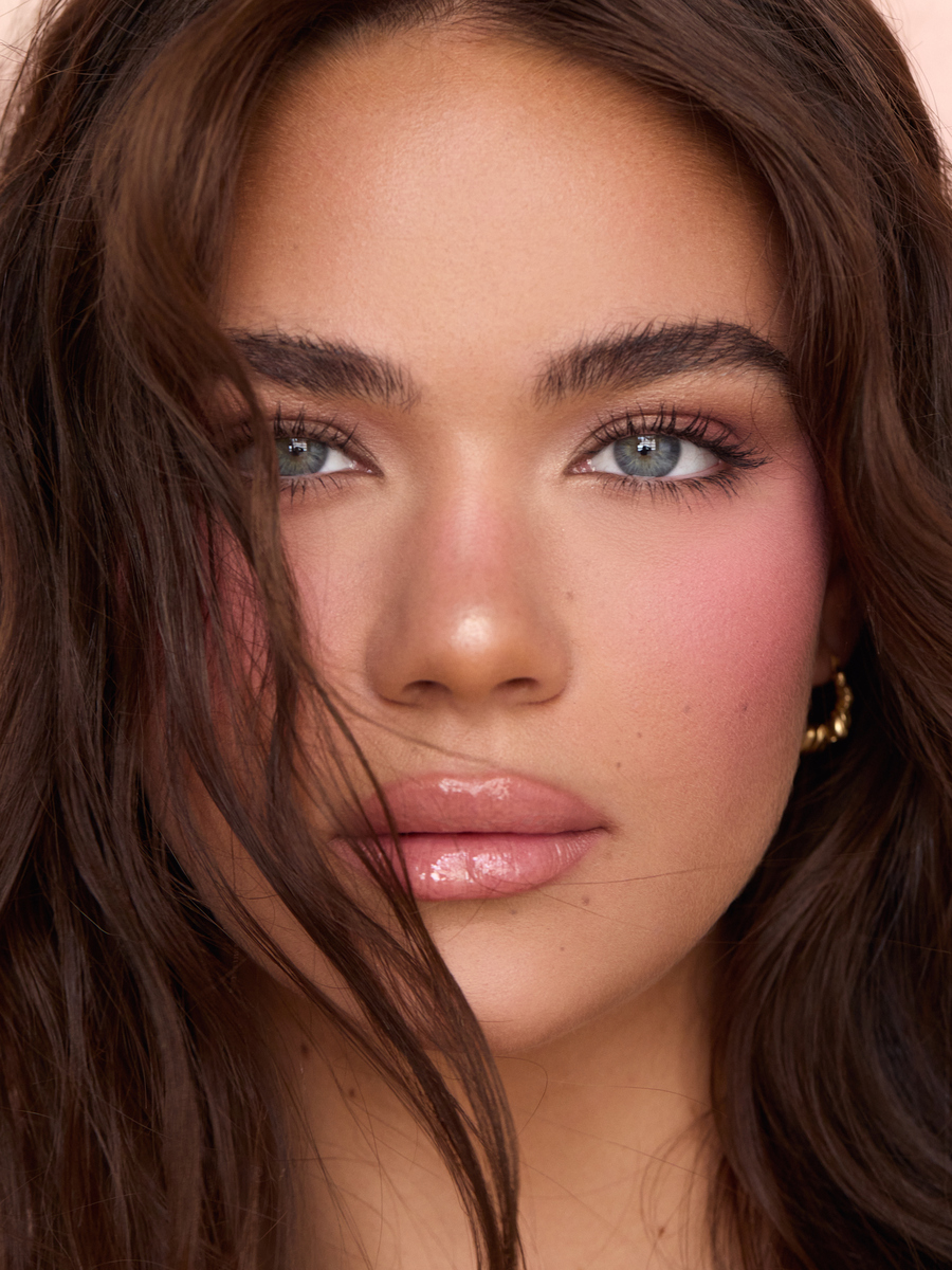Close-up glam beauty portrait of a brunette model wearing rosy pink blush, defined lashes, and glossy pink lips, photographed in Miami by Josh Eskridge.